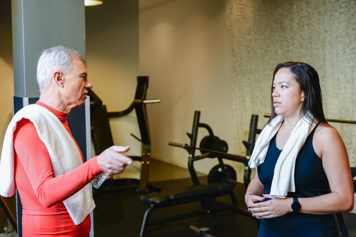 A trainer having a warm, relaxed conversation with an older adult before a stability session in comfortable clothing.